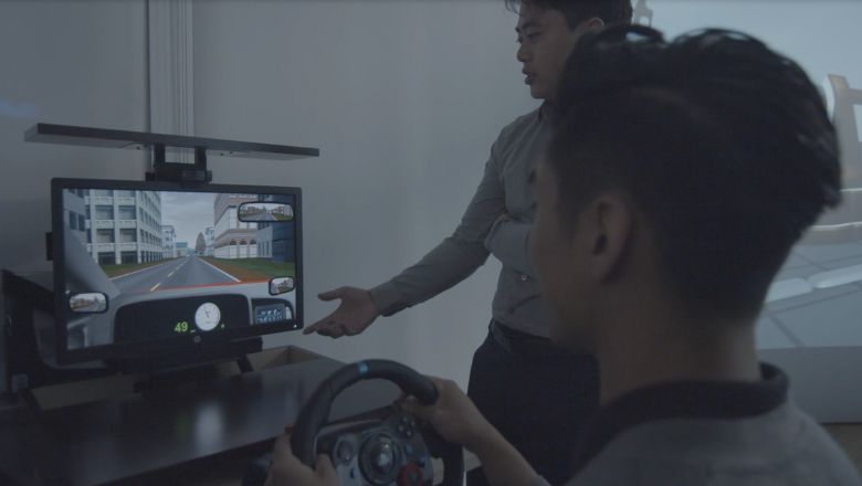 A student playing a video game with a steering wheel controller.