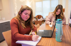 Two students work on homework together at a kitchen table area.