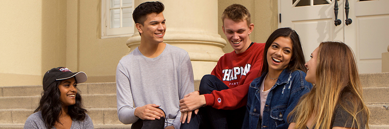 five students sitting in front of a building smiling and talking
