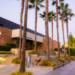 Students sit on steps outside of campus building surrounded by palm trees
