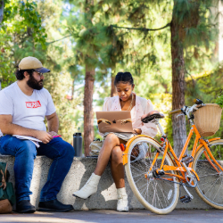 Students sit outdoors on campus near bike