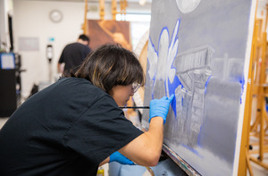 A student paints on a canvas.