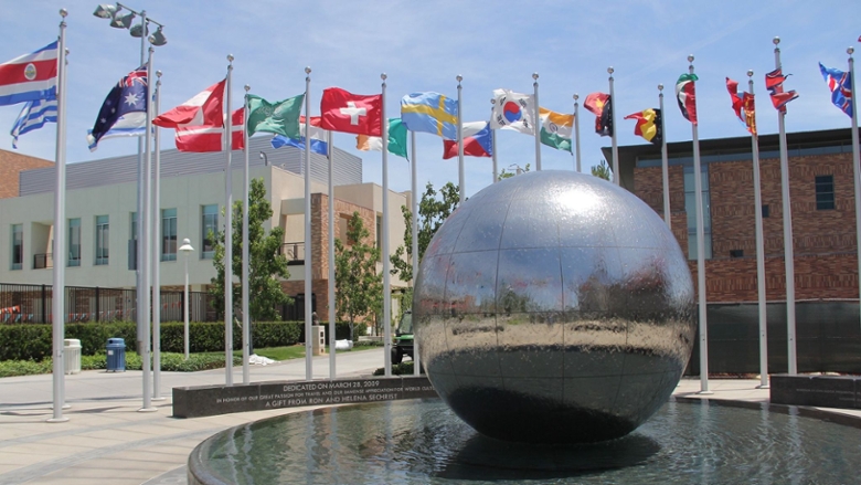 Flags from various countries fly around a fountain with a spherical metallic sculpture at its center in the Global Citizens Plaza at Chapman University