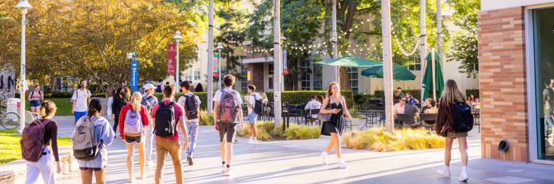 Students walking outside of Beckman Hall on a sunny day.