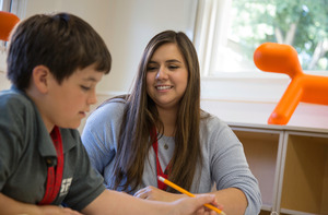 A student teacher works in an elementary aged student in a classroom.