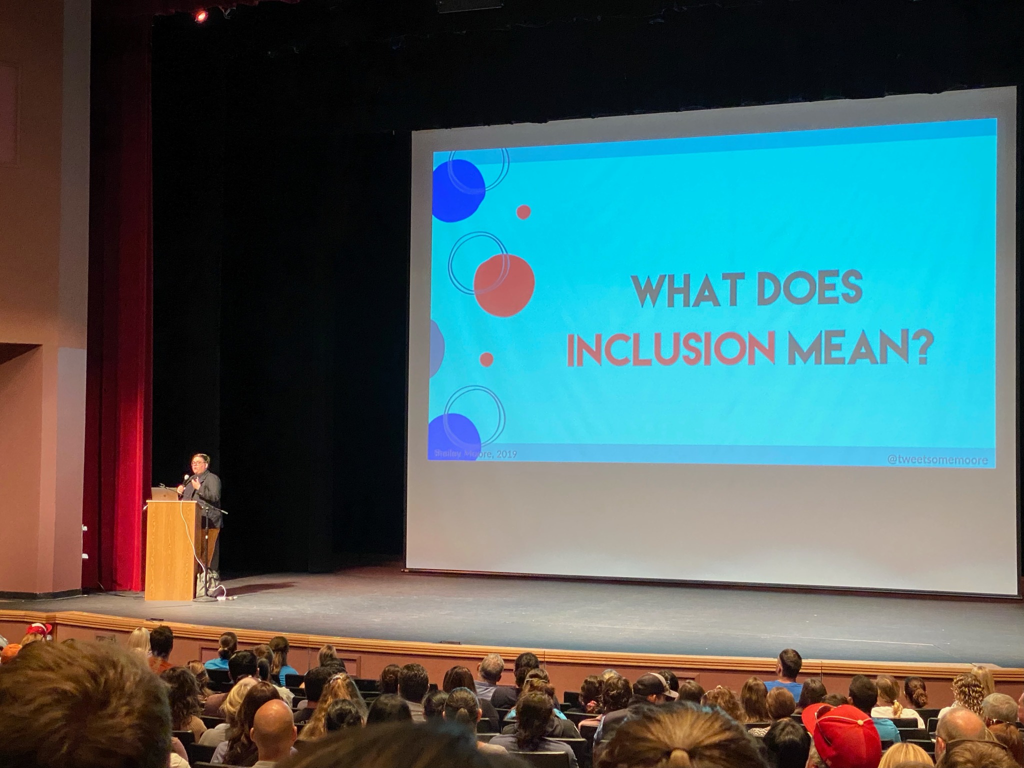 Shelley Moore is presenting the keynote on stage with "What Does Inclusion Mean" written on the large screen on stage.
