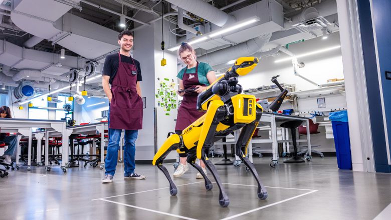Two students surrounding a yellow robotic dog.