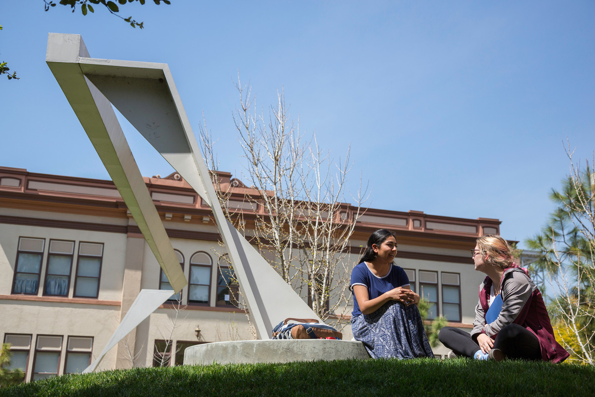 Two students have a discussion near an abstract sculpture.